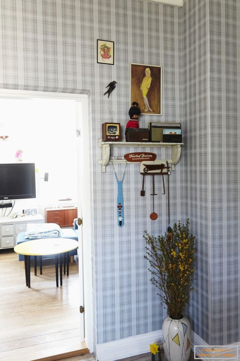Chodba s kostkovanou tapetou, podlahovou vázou pod deskou, vedle otevřených dveří do obývacího pokoje