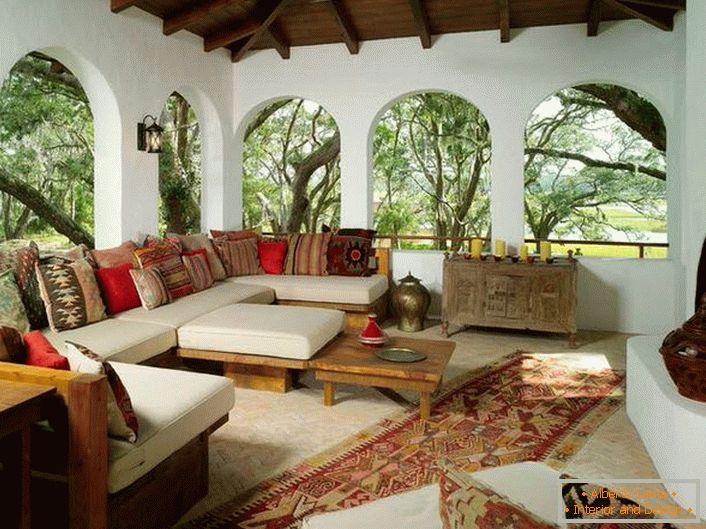 Veranda venkovského domu je zařízena podle středomořského stylu. Zajímavostí je dekor s množstvím barevných polštářů.