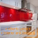 Bílý nábytek a červená zástěra v interiéru kuchyně