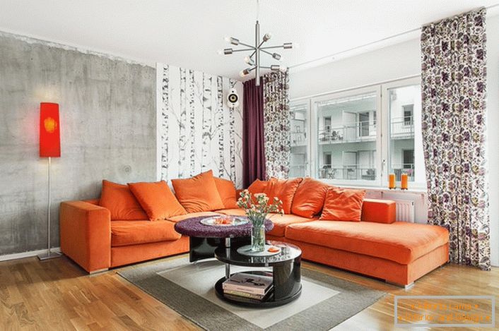 Skandinávský styl je spojen s použitím teplých barev v interiéru. Měkká oranžová pohovka organicky vypadá na pozadí stěn studeně šedé barvy.