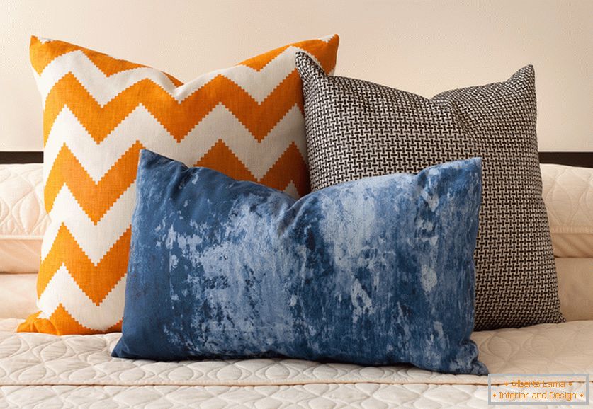 Jasné oranžové, modré a černobílé dekorační polštáře se zajímavými tisky na posteli