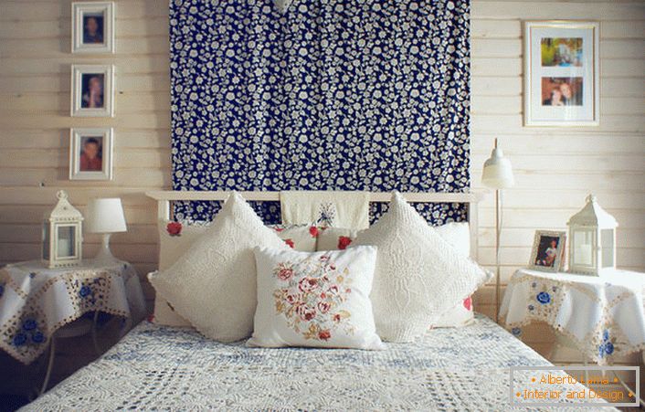 V souladu s rustikálním stylem je postel zdobena řadou polštářů s kontrastní červenou výšivkou. Noční stolky jsou pokryté ubrusem s jemnými modrými květy.