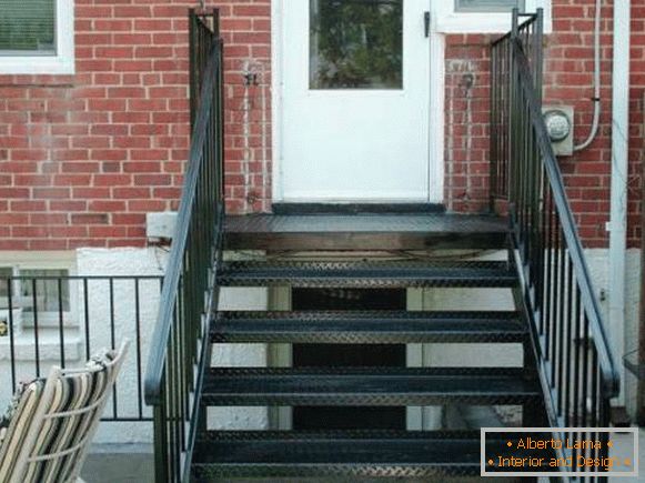 Malá kovová veranda se schodištěm do cihlového domu