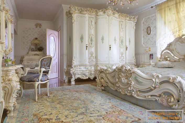 Sněhově bílá ložnice s vyřezávaným masivním nábytkem ze dřeva. Lůžko s vysokou čelní deskou na čelní straně, elegantně zapadá do interiéru v barokním stylu.