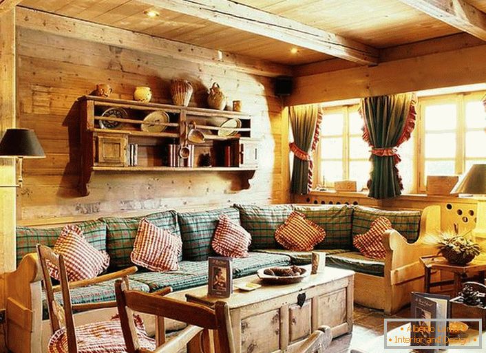 Dřevěné dekorace na stěnu, kontrastní polštáře na měkké pohovce, husté závěsy s volánky na oknech. Útulný obývací pokoj v rustikálním stylu ve venkovském domě.