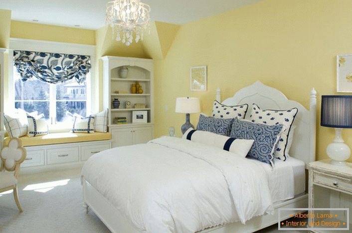 Vybledlá žlutá barva dokončuje harmonii s bílými a modrými prvky dekoru. Neobvyklá kombinace je odvážným řešením pro ložnici ve venkovském stylu.