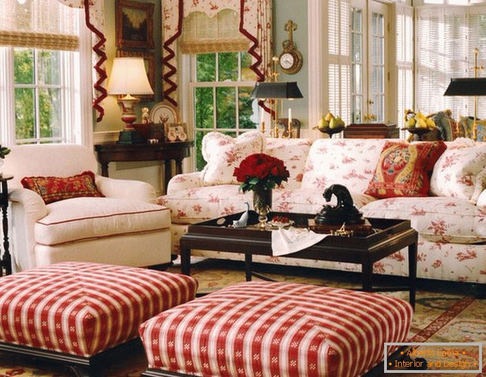 Jednoduchý, skromný a útulný obývací pokoj v anglickém stylu v malé venkovské budově. Akcenty červené dělají atmosféru v místnosti uvolněnou a veselou.